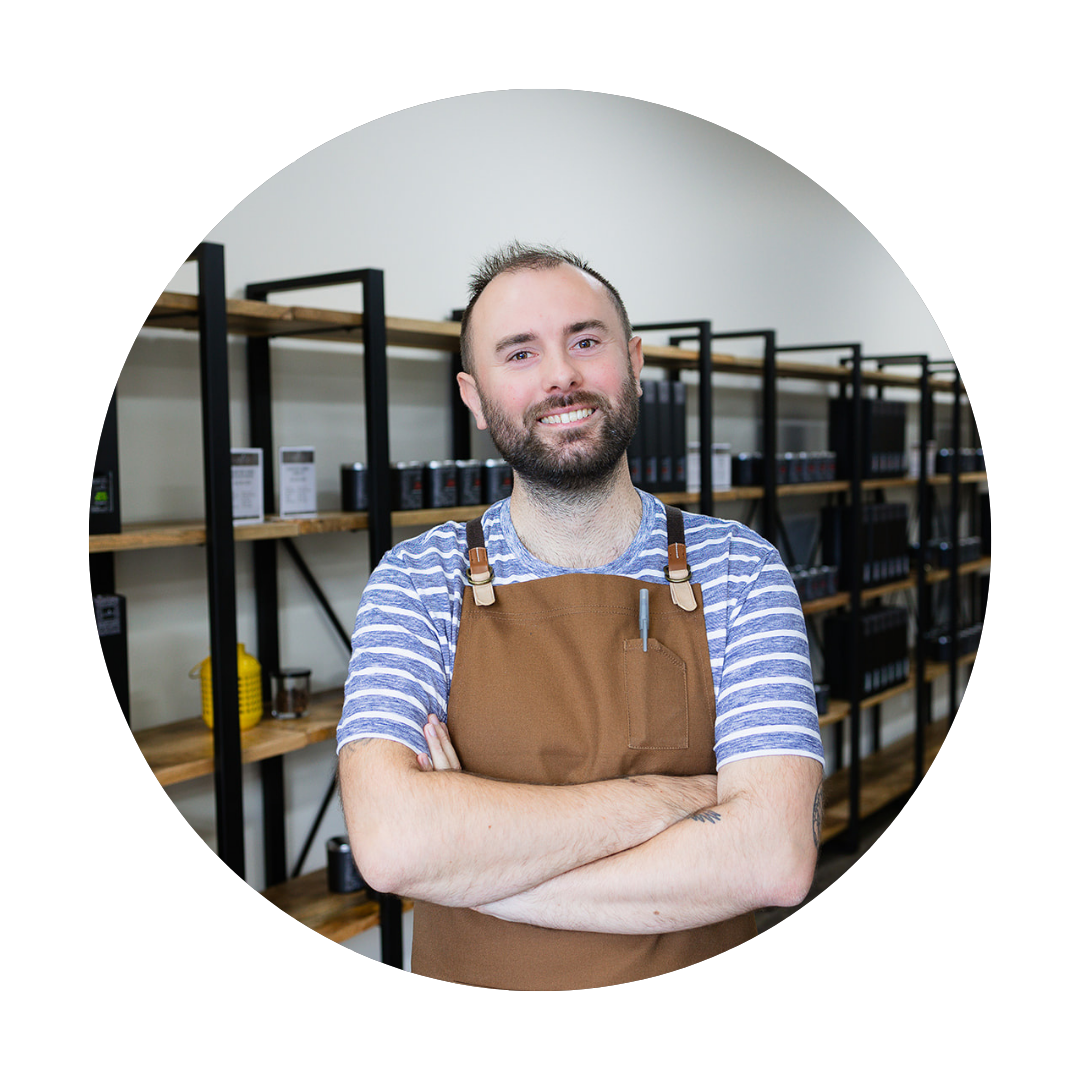 Photo of Jacob Jollymore, the Scentertainment Director & Brand Glow-Getter at Lunico Candle Co. He is standing with his arms crossed, with shelves of candles and reed diffusers in the background.