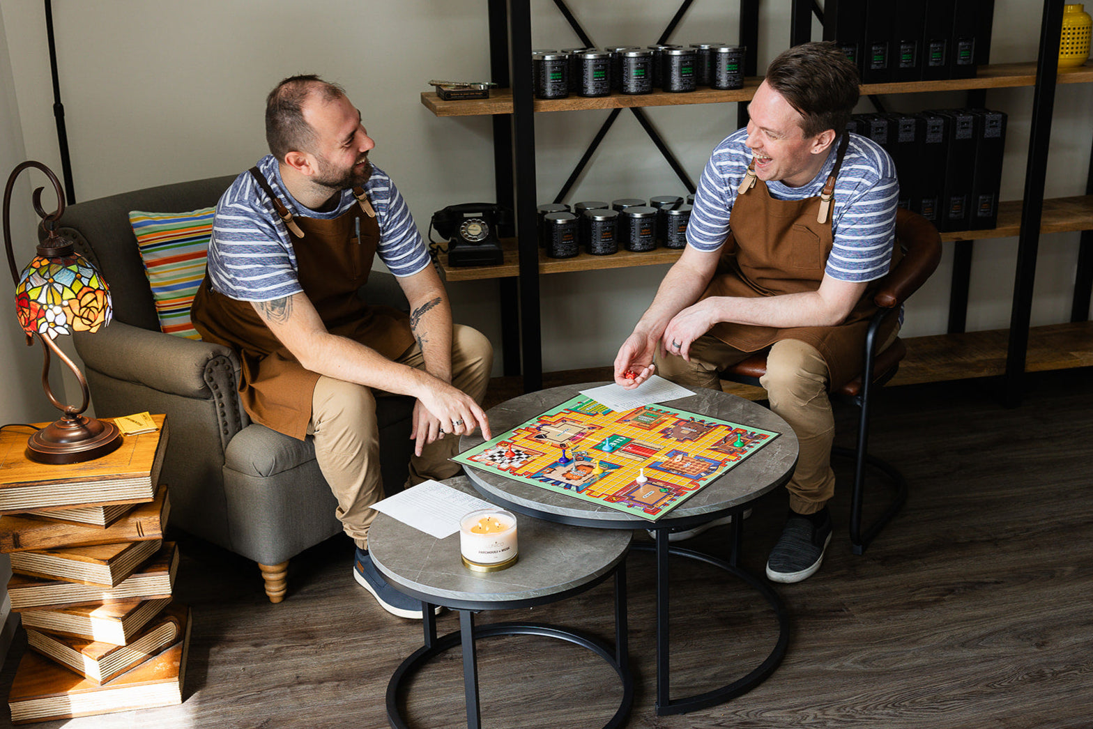 William and Jacob are playing Cluedo in the candle shop. They are in uniform and laughing at each other.