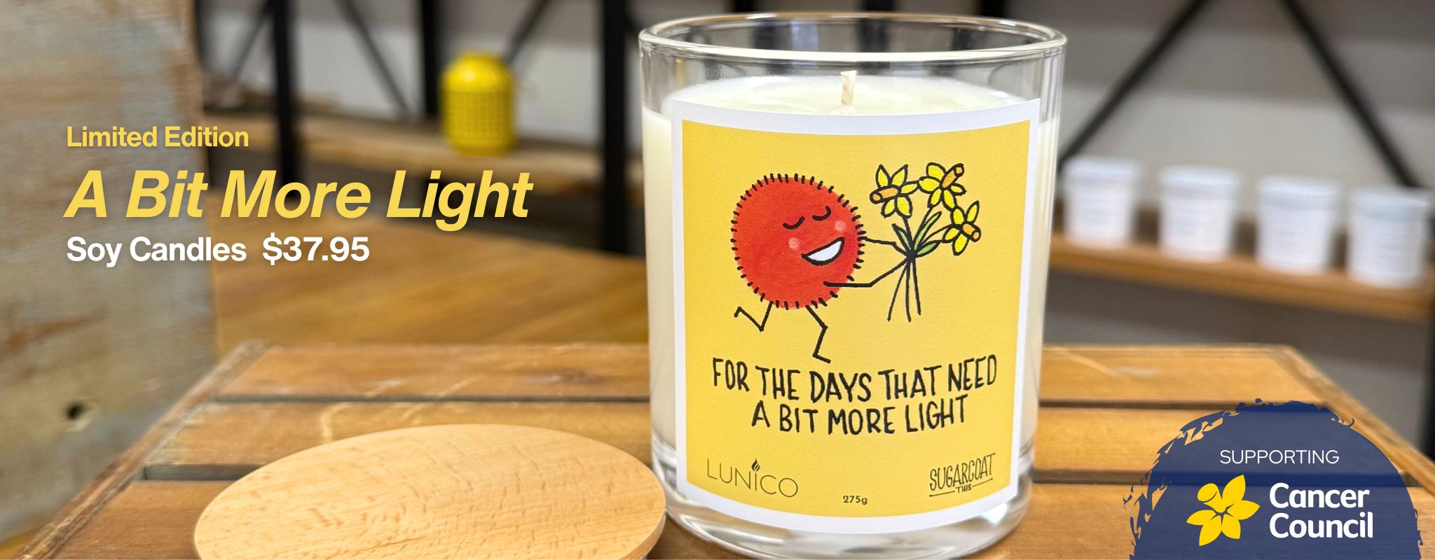 Candle with a yellow label on a wooden surface, with text about the product and supporting organization.